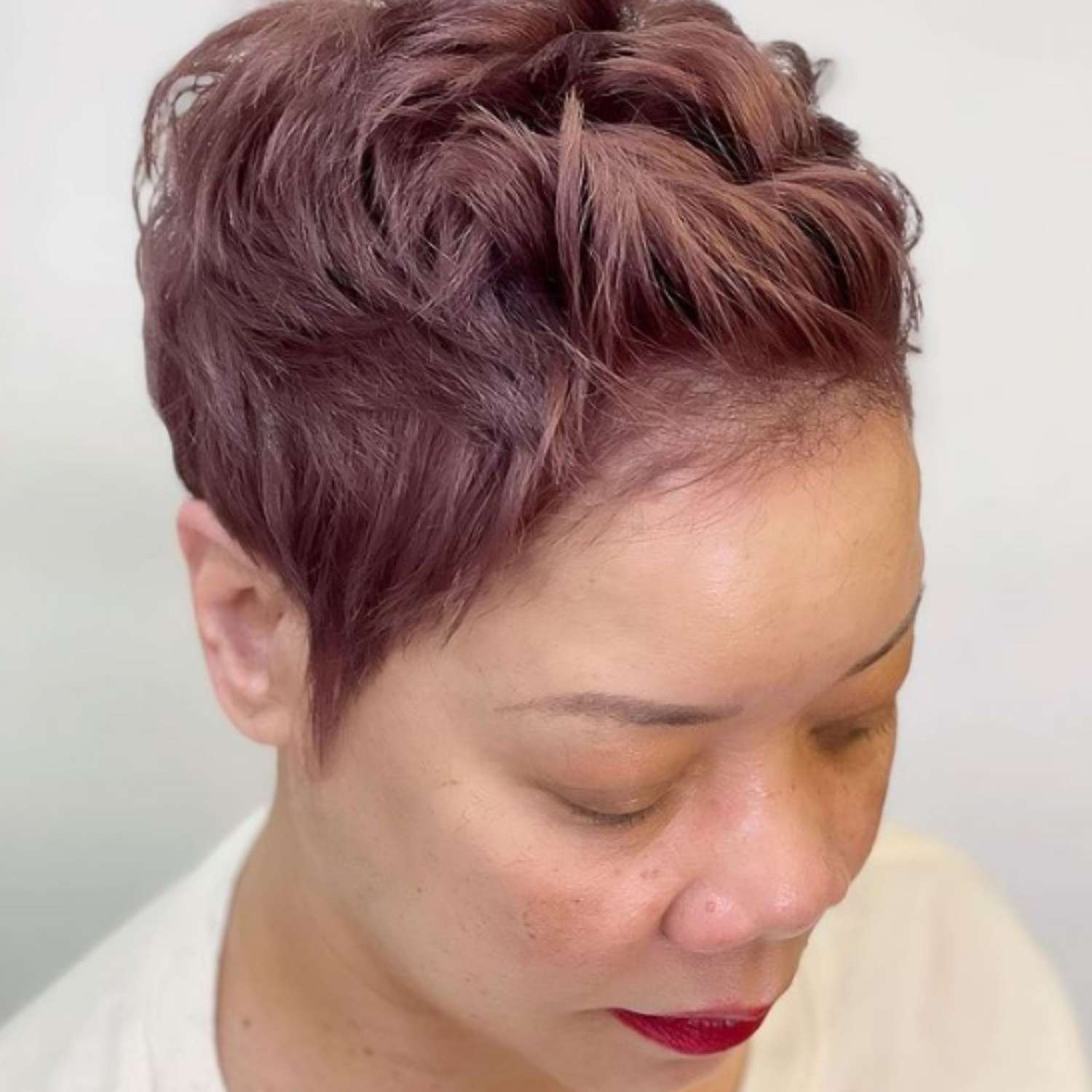 Close cropped hairstyle with muted pink-auburn hair.